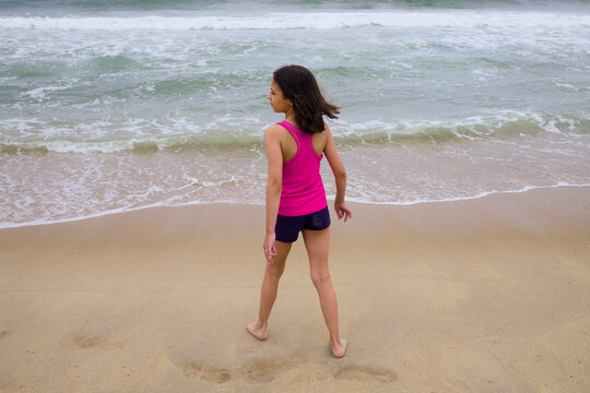 Girl looks toward ocean surf on sandy shoreline