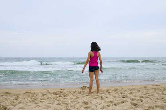 Young girl stands at the edge of waves on sandy beach