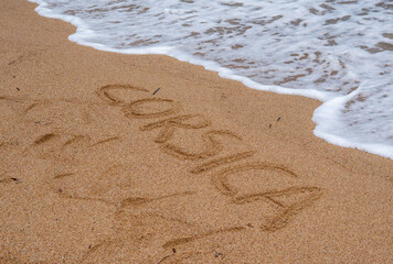 footprint on the sand with waves and the word Corsica written in the sand 