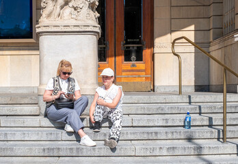 A young woman and a girl of 10 years old, Caucasian, sit and rest on the steps of the Royal Theatre in Stockholm.