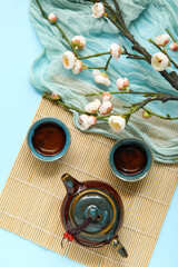 Bamboo with teapot, cups of tea and blossoming branches on blue background