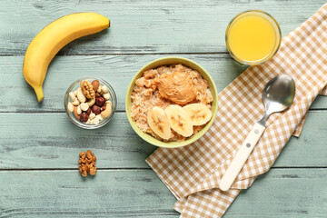 Bowl with tasty oatmeal, banana, peanut butter, nuts and glass of juice on wooden background