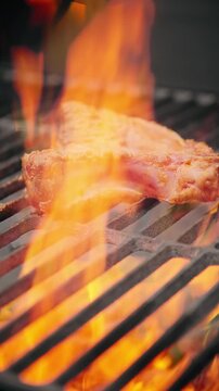 Close-up of raw pork rib cooking over bright orange flames on a barbecue grill with hot charcoal beneath.