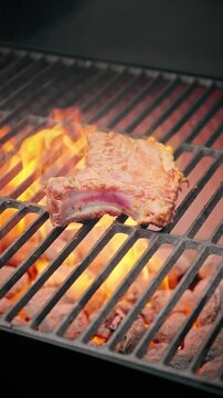 Close-up of raw pork rib cooking over bright orange flames on a barbecue grill with hot charcoal beneath.
