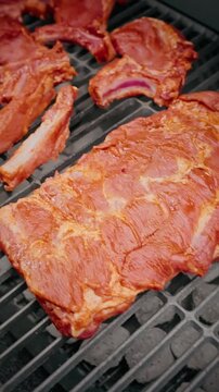 Close-up of raw marinated pork ribs placed on a barbecue grill, ready for cooking over hot charcoal.