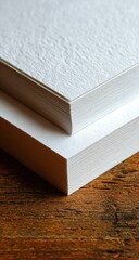 Close-up of two stacks of textured white paper sheets on wood