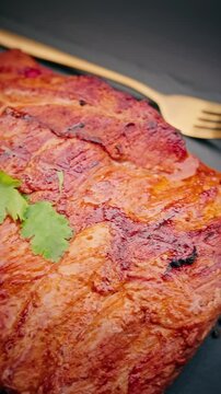 Juicy grilled pork ribs served on black slate plate with fresh cilantro garnish and chopped green herbs in a bowl.