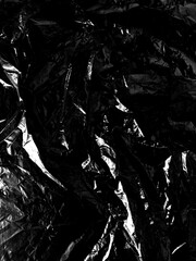 Transparent cellophane bag against a sleek black background, showcasing its glossy, delicate texture. The wrinkled and tattered plastic surface creates an intriguing abstract pattern, highlighting.