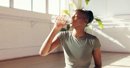 Black woman, drinking and water bottle in studio for hydration, recovery or natural beverage. Female person, yogi or thirst with mineral liquid for fitness, rest or workout break in health club