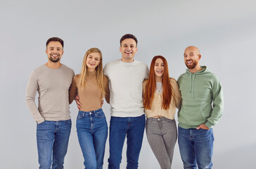 Obraz premium Indoor group portrait of 5 happy, joyful adult male and female friends. Five cheerful, smiling people wearing casual clothes standing together by a light gray wall