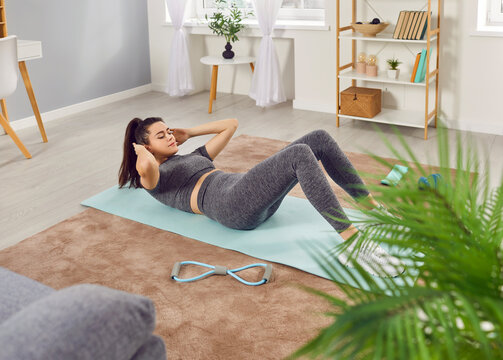 Sporty focused young woman in sportswear having fitness workout at home, doing sit ups on yoga mat in living room. Athletic slim Caucasian girl strengthening her body and maintaining healthy routine. - Powered by Adobe