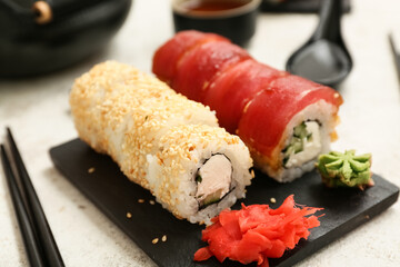 Board with tasty sushi rolls, marinated ginger and chopsticks on white grunge background, closeup