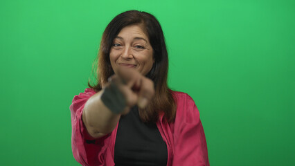 Woman wearing pink jacket smiling and pointing finger to camera on green screen in studio; invitation.