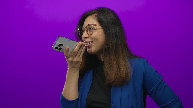 Woman holding smartphone speaks into device in purple studio sending voice message clearly; communication. - Powered by Adobe