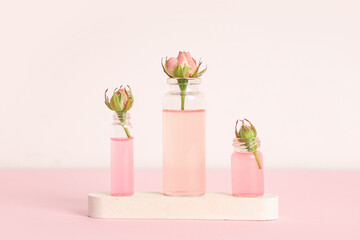 Composition with bottles of cosmetic oil, plaster stand and roses on pink background