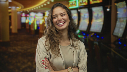Woman with arms crossed at a slot machine inside a casino building wearing a beige blouse and...