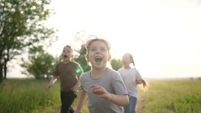 Children run across grassy field child and kid run through tall grass outdoor play under sunlight showing happy expression friendship and smile as three children enjoy playful motion together
