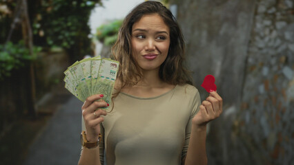 Woman holding argentinian pesos and heart outdoors with a thoughtful expression, blending money and...