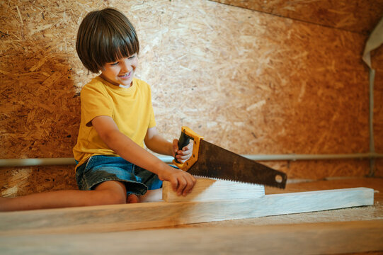 Smiling child in yellow shirt sawing wood during home renovation indoors