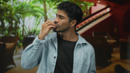 Man makes chef kiss gesture with fingertips to lips and smiles in hotel lounge setting; approval perfection.