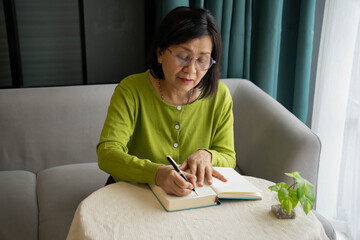 Mature Asian Woman Writing Daily Diary at Home for Personal Reflection.