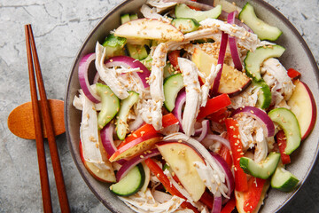 Diet salad with shredded chicken, cucumber, apple, red onion, bell pepper and sesame seeds in Asian style close-up in a bowl on the table. Horizontal top view from above