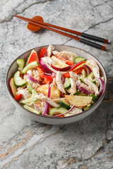 Korean chicken salad combines with shredded poached meat, cucumber, onion, pepper and apple slices are dressed with a tangy sesame mustard dressing closeup on the plate on the table. Vertical