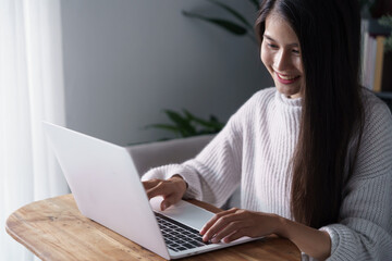 Naklejka premium Asian woman sits on sofa using laptop in living room