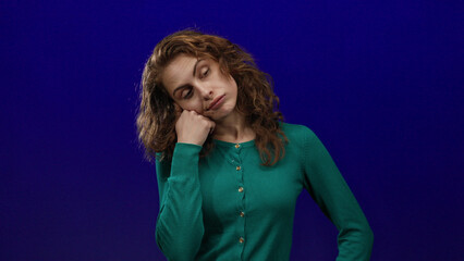 Woman expressing boredom over isolated blue background, wearing a green sweater and showcasing a contemplative mood.