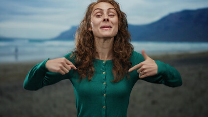 Woman gesturing energetically on a beach with mountains in the background, emphasizing...