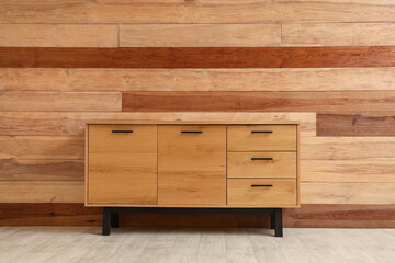 Stylish cabinet near brown wooden wall in room