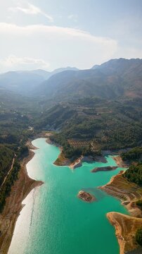 Drone video of the turquoise Guadalest Reservoir in Spain, surrounded by green hills and mountains, showing vivid water colors and scenic Mediterranean landscapes.