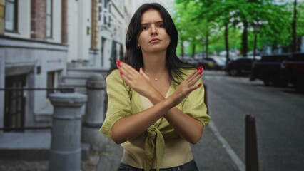 Fototapeta premium Hispanic woman standing with crossed arms on street outside classic building in daylight; rejection.