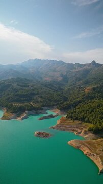 Drone video of the turquoise Guadalest Reservoir in Spain, surrounded by green hills and mountains, showing vivid water colors and scenic Mediterranean landscapes.