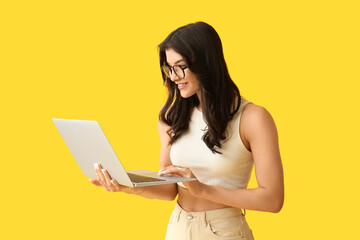 Beautiful young happy woman working with laptop on yellow background