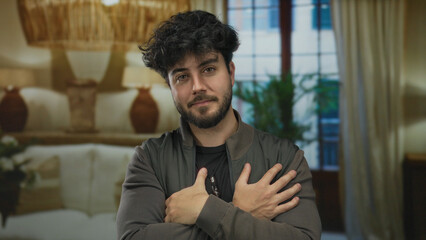 Young man with beard crossing arms in cozy hotel room with warm lighting and elegant decor,...