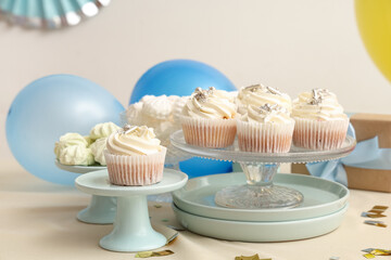 Dessert stands with tasty white cupcakes, decor and other sweets for birthday party on table