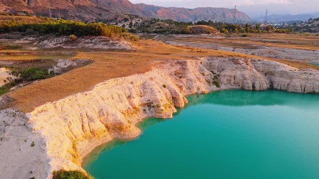 Drone video showing turquoise waters and rocky shoreline in Spain, with golden hour sunlight highlighting the rugged cliffs and surrounding landscape.