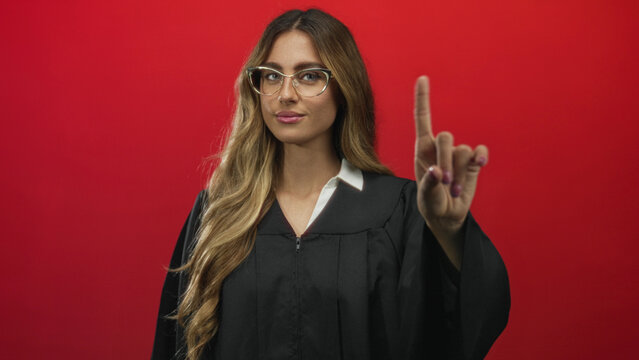 Judge woman wearing black robe pointing finger upward in studio with confident expression; authority decision guidance.