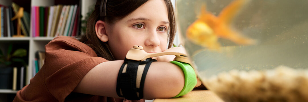 Contemplative child with arm prosthesis watching goldfish at home