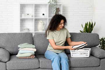 Beautiful young happy African-American woman folding clean clothes at home