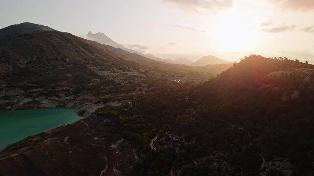 Drone video showing a mountain forest in Spain at sunset, with soft golden light filtering through hills and trees, creating a peaceful and warm atmosphere.