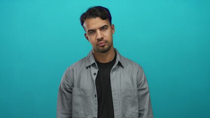 Young hispanic man making gun gesture with fingers in front of isolated green background displaying...