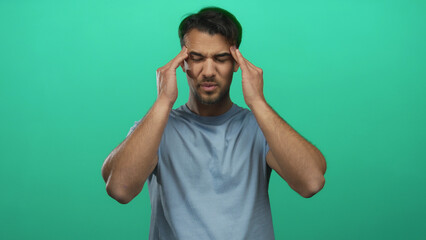 Young hispanic man with headache stands against an isolated green background, expressing discomfort...