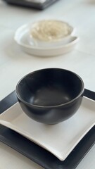 Minimalist Black Ceramic Bowl on White Square Plate with Elegant Modern Table Setting in Contemporary Home Interior