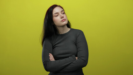 Woman with brunette hair stands confidently against a bright yellow background with arms crossed,...