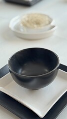 Minimalist Black Ceramic Bowl on White Square Plate with Elegant Modern Table Setting in Contemporary Home Interior