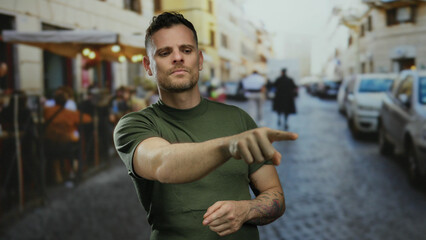 Man in green shirt with tattoos pointing on lively urban street with blurred people and vehicles in...