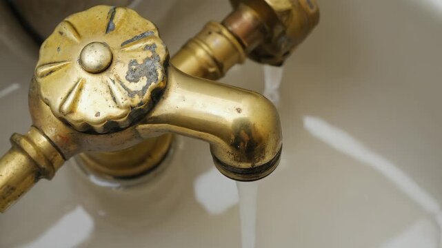 Close-up shot of an antique brass faucet with water flowing into a porcelain sink, depicting plumbing and vintage design
