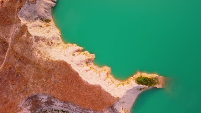 Drone video captures a rocky shoreline with green vegetation surrounded by bright turquoise waters of a lake in Spain, viewed directly from above.